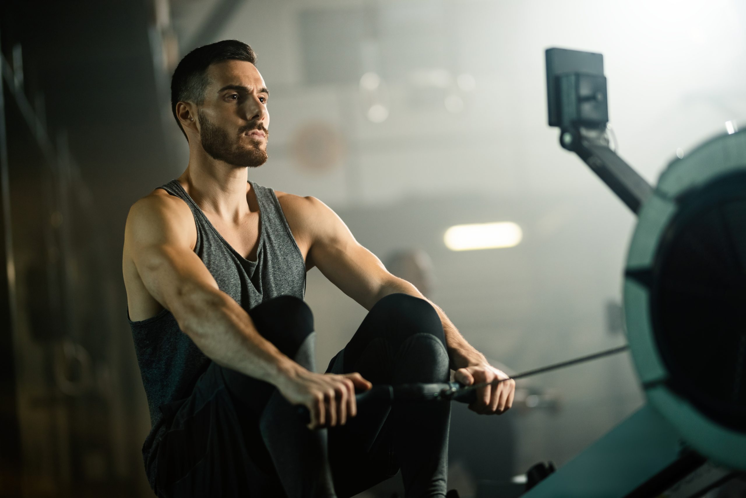 Young sportsman working out on rowing machine in a gym.
